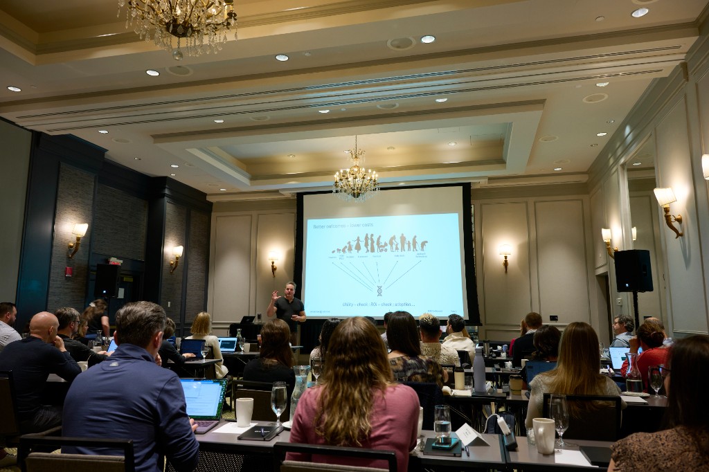 Inflection Medicine presentation to an audience in a conference room, with a speaker beside a projected slide.